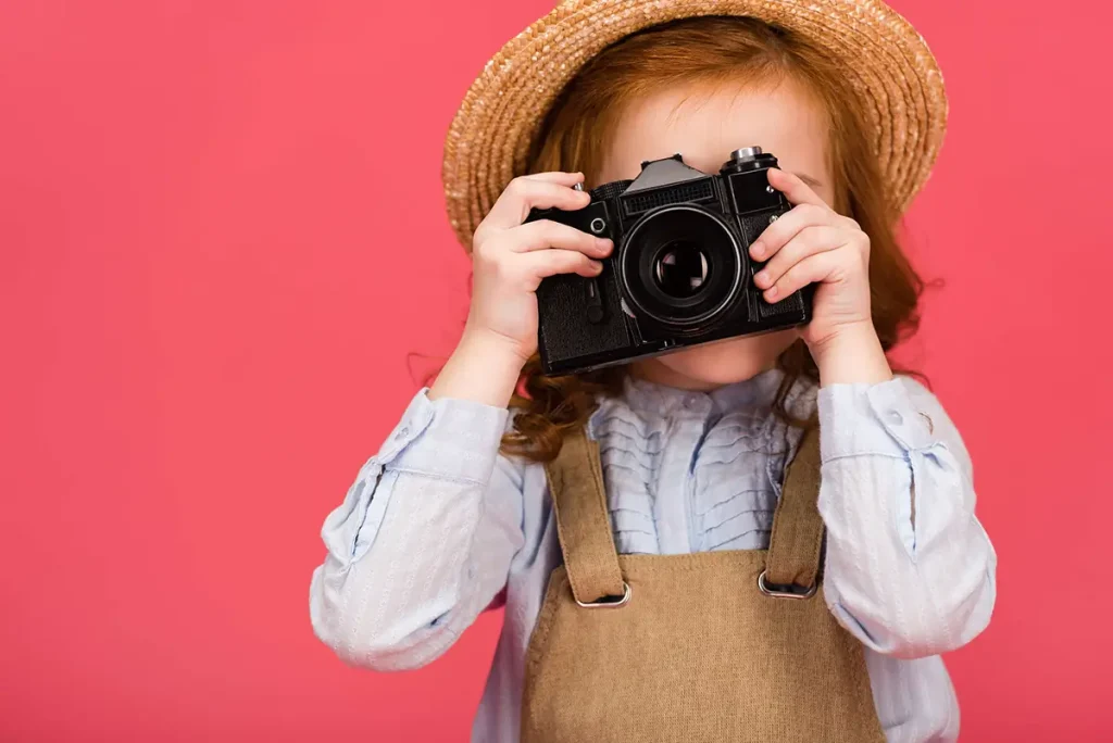 Child with straw hat holding an old camera